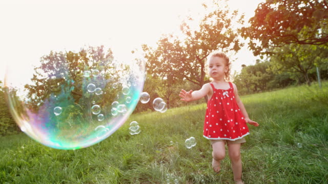 SLO MO Little toddler girl in red tunic catching soap bubbles in the orchard