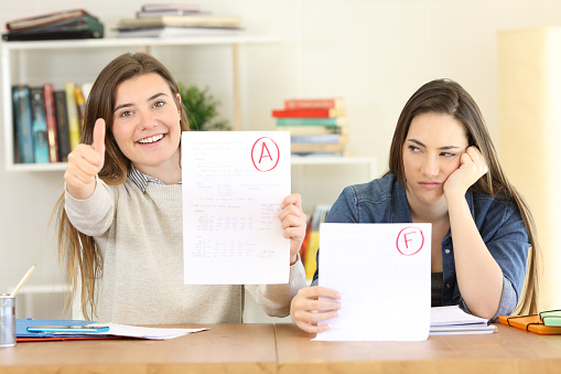 Front view portrait of two students showing failed and approved exams at home