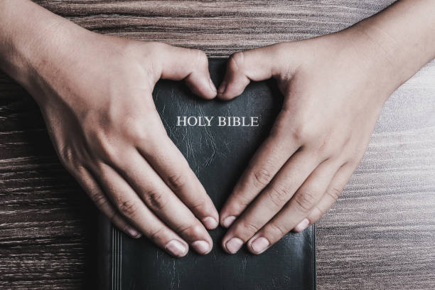 istock Holy bible with heart shape hands 1003824098