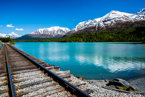 Railroad track by the turquoise Lower Trail Lake in the Chugach National Forest, Alaska, with mountain range in background