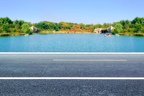 istock Blue sky and white clouds, lake scenery and asphalt pavement, automobile advertising background road materials 1003912796