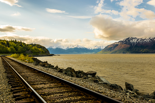 Part of Alaska railroad in the Chugach National Forest with mountain range and Turnagain arm in background.