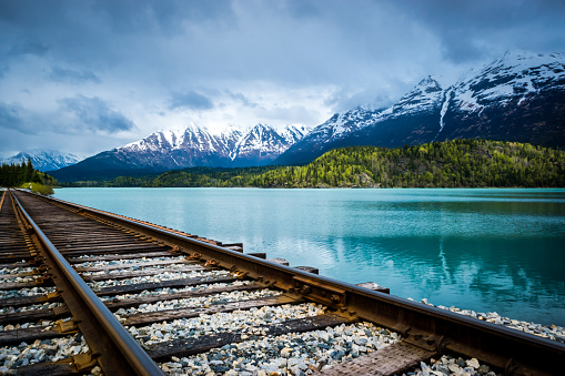 Railroad track by the turquoise Lower Trail Lake in the Chugach National Forest, Alaska, with mountain range in background