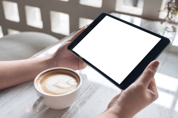 istock Mockup image of a woman holding black tablet pc with white blank screen with coffee cup on table 1003943378