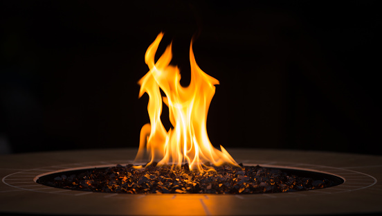 Close up of an outdoor fireplace with a big yellow flame and black background