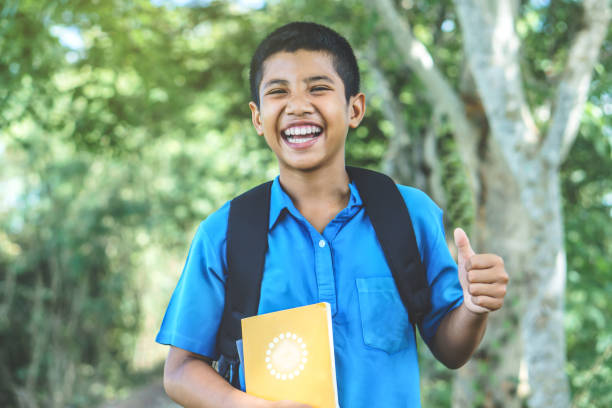 学校手本を押しながら笑顔に戻ってアジアの少年の幸せな学生 - thumbs up book smiling student ストックフォトと画像