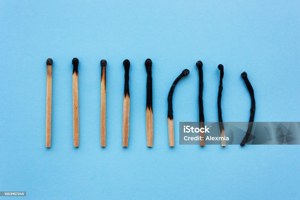 Burned matches in a row on a blue background. Burned matches in a row on a blue background. The concept of depression, extinction, illness, burnout, aging. View from above, flat Mental Burnout Stock Photo