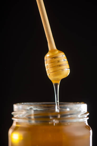 istock Organic honey drips from wooden dipper in jar 1003976762