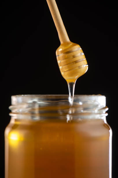 istock Organic honey drips from wooden dipper in jar 1003976788