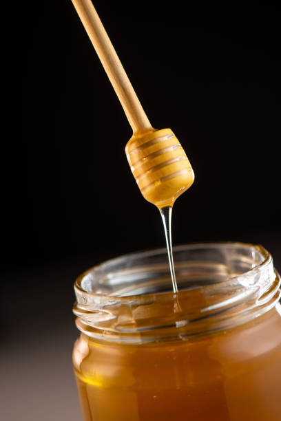 istock Organic honey drips from wooden dipper in jar 1003976814