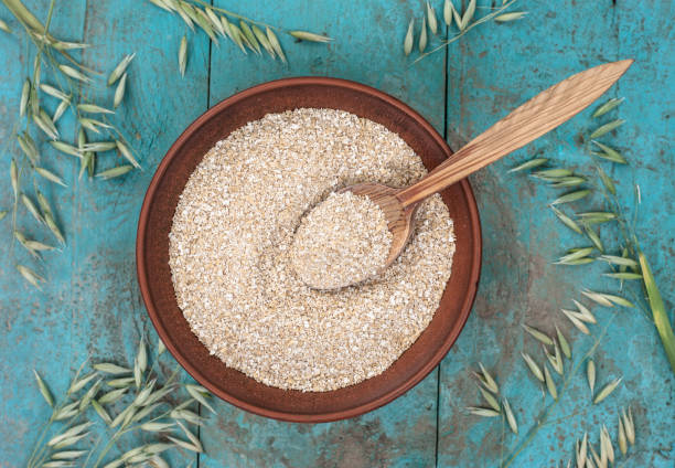 Oat bran Oat bran in a rustic style in a plate with a spoon, on a blue plaque background with ears bran stock pictures, royalty-free photos & images