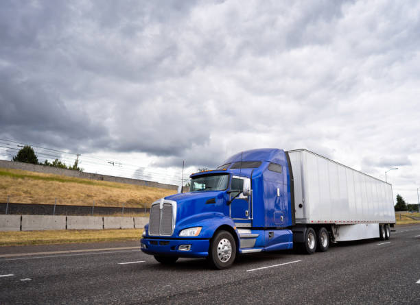 classico semicarro big rig blu con semirimorchio a secco che va su un'ampia autostrada con cielo tempestoso - corsa di superstrada foto e immagini stock