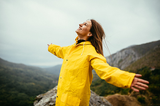 One woman, standing on mountain on a rainy day in yellow raincoat.