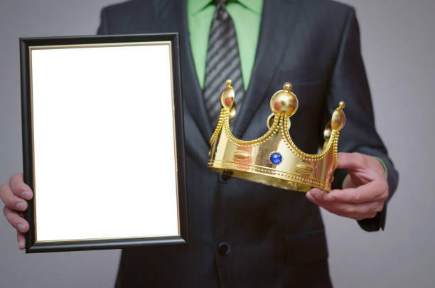 Businessman. Winner blank diploma or certificate mockup in businessman hand. Man is holding a blank photo frame with copy space for human face and a golden crown above it. person holding frame over face stock pictures, royalty-free photos & images