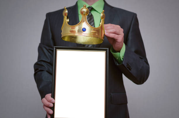 Businessman. Winner blank diploma or certificate mockup in businessman hand. Man is holding a blank photo frame with copy space for human face and a golden crown above it. person holding frame over face stock pictures, royalty-free photos & images
