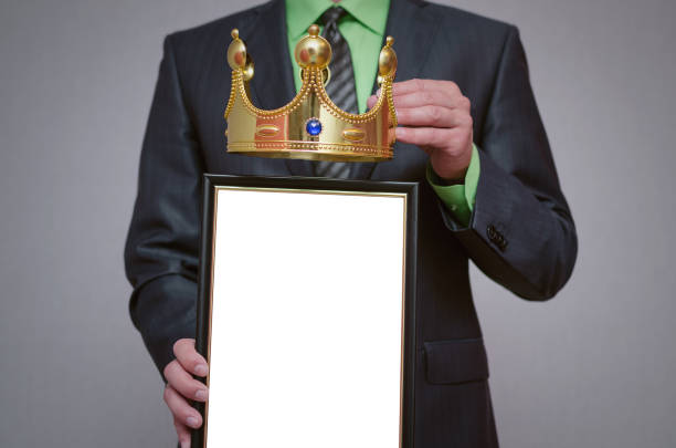 Businessman. Winner blank diploma or certificate mockup in businessman hand. Man is holding a blank photo frame with copy space for human face and a golden crown above it. person holding frame over face stock pictures, royalty-free photos & images