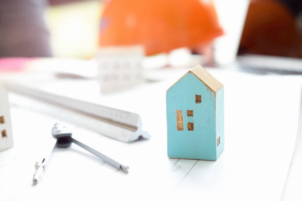 istock House model on table in office with blueprints,engineer inspection in workplace for architectural plan,sketching a construction project ,selective focus,Business construction concept. 1003992236
