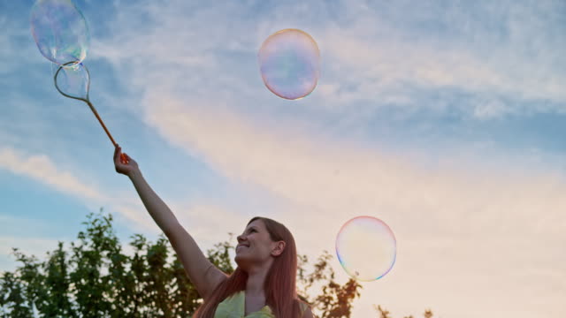 SLO MO Young woman making large soap bubbles and smiling