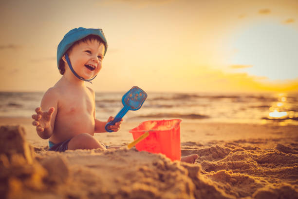 Cute child standing near sandcastle by the sea in the evening