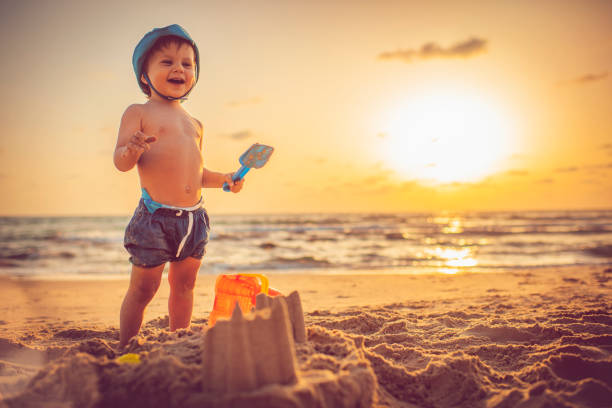 glückliche kleine junge gebäude sandburg am strand im sonnenuntergang - lifestyles child beach digging stock-fotos und bilder