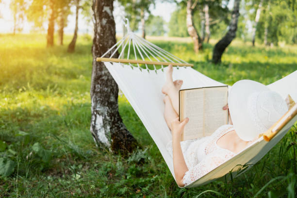 Senior Woman Relaxing Outside In Hammock With Book