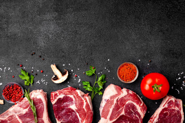 istock Meat raw steaks lie on a black background with vegetables, tomatoes, marasmade, mushrooms. background image. side view, copy space, top view 1004022648
