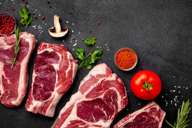 istock Meat raw steaks lie on a black background with vegetables, tomatoes, marasmade, mushrooms. background image. side view, copy space, top view 1004022660