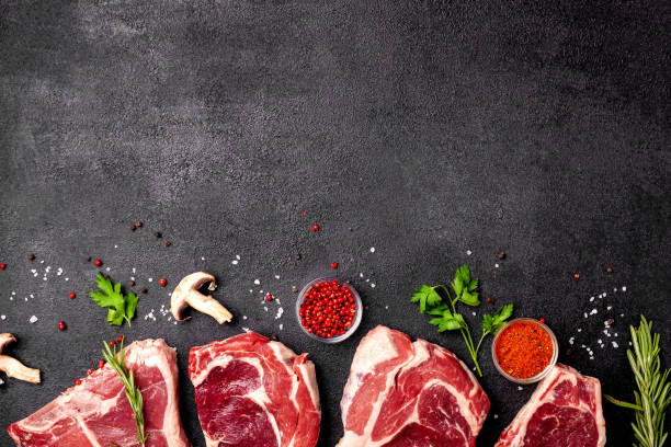 istock Meat raw steaks lie on a black background with vegetables, tomatoes, marasmade, mushrooms. background image. side view, copy space, top view 1004022664