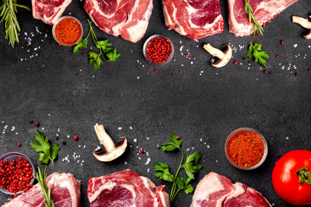 istock Meat raw steaks lie on a black background with vegetables, tomatoes, marasmade, mushrooms. background image. side view, copy space, top view 1004022668