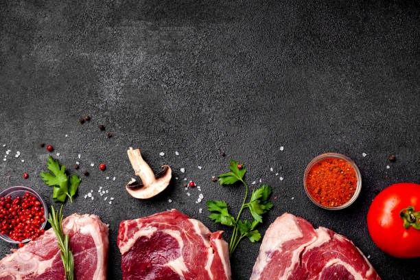 istock Meat raw steaks lie on a black background with vegetables, tomatoes, marasmade, mushrooms. background image. side view, copy space, top view 1004022678