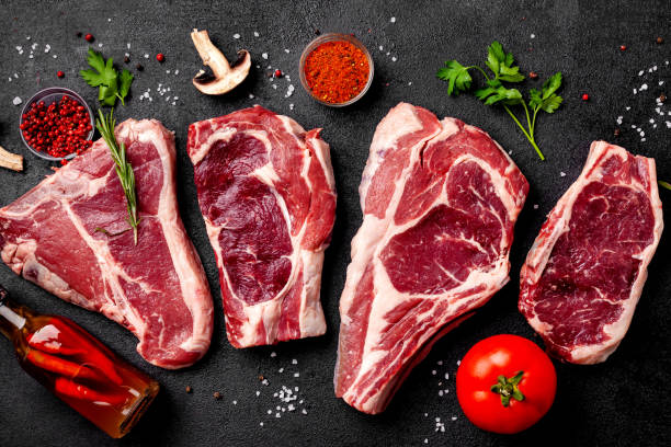 istock Meat raw steaks lie on a black background with vegetables, tomatoes, marasmade, mushrooms. background image. side view, copy space, top view 1004022680