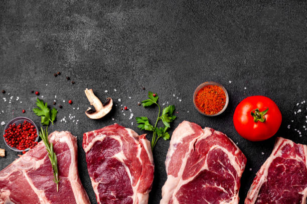 istock Meat raw steaks lie on a black background with vegetables, tomatoes, marasmade, mushrooms. background image. side view, copy space, top view 1004022682
