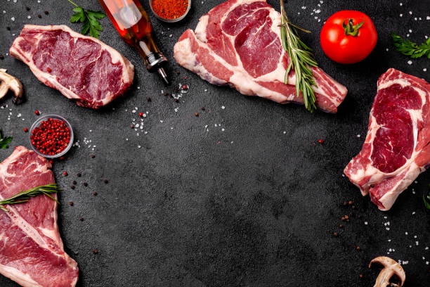 istock Meat raw steaks lie on a black background with vegetables, tomatoes, marasmade, mushrooms. background image. side view, copy space, top view 1004022684