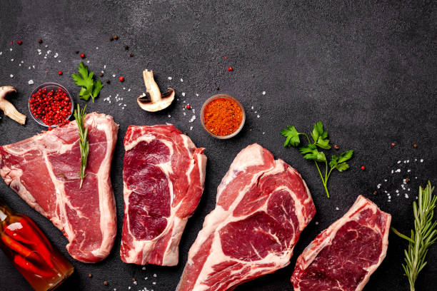 istock Meat raw steaks lie on a black background with vegetables, tomatoes, marasmade, mushrooms. background image. side view, copy space, top view 1004022698
