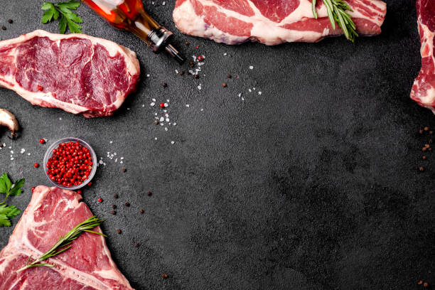 istock Meat raw steaks lie on a black background with vegetables, tomatoes, marasmade, mushrooms. background image. side view, copy space, top view 1004022702
