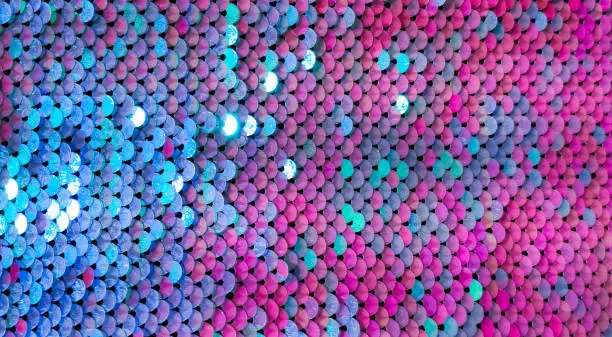 Abstract colorful Texture scales with bright Sequins close-up. Glamor Background with shiny blue, purple and Magenta sequins on fabric, macro. Beautiful Holiday Wallpaper with pattern of round Sequins