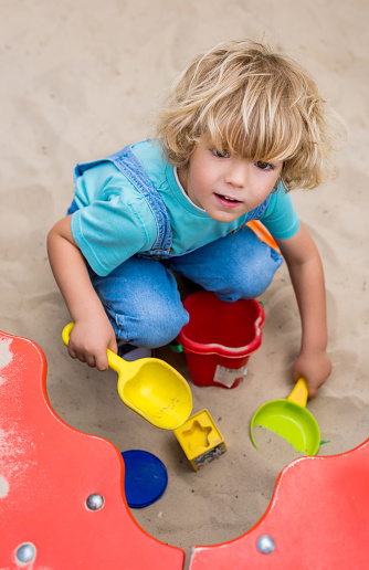 high angle view of little boy playing with plastic scoops, molds and bucket in sandbox at playgorund