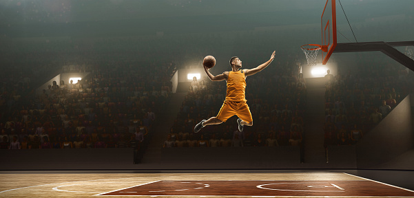 Young muscular basketball player with a ball on floodlight professional court scoring a goal