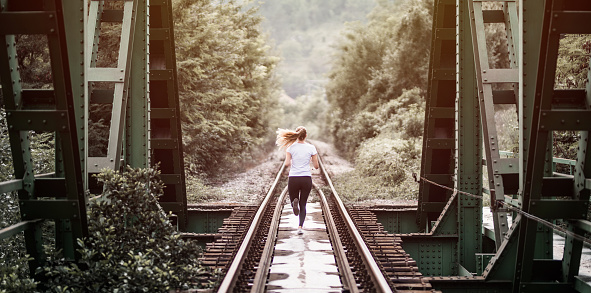 Young woman running on the railroad track through the forest