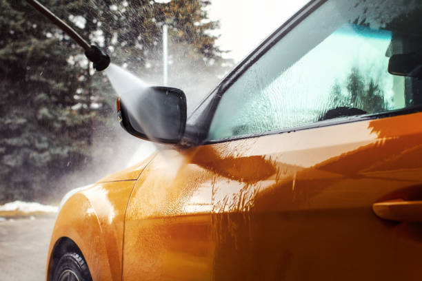 Detail on dark yellow car front mirror being washed with jet water stream in carwash. stock photo