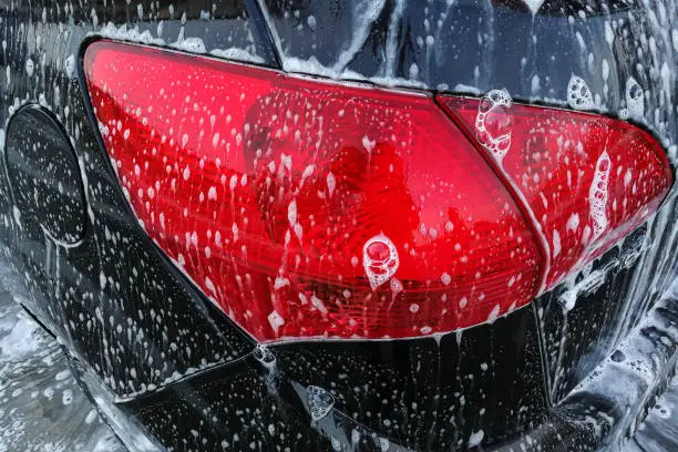 Photo of Detail photo of brown car rear red light covered with soap foam when being cleaned in carwash.