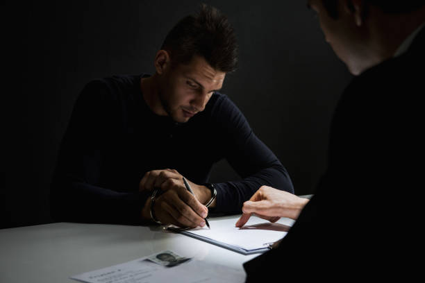 istock Criminal man with handcuffs signing document in interrogation room 1004108434