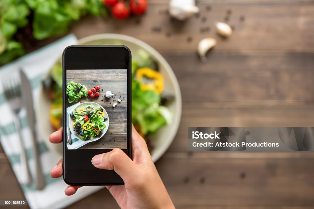 Hand holding smartphone taking photo of beautiful food, mix fresh green salad Food blogger using smartphone taking photo of beautiful mix fresh green salad on wood table to share on social media Food Stock Photo