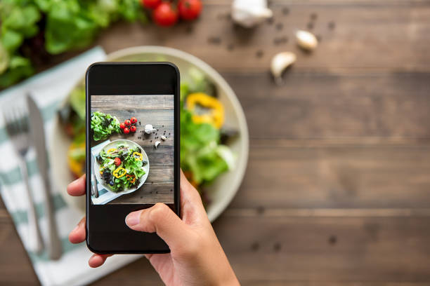 Hand holding smartphone taking photo of beautiful food, mix fresh green salad Food blogger using smartphone taking photo of beautiful mix fresh green salad on wood table to share on social media networking photos stock pictures, royalty-free photos & images