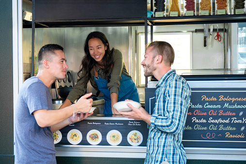 Two friends enjoy eating pasta at counter of food truck
