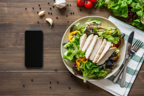 gesunde hähnchensalat neben smartphone auf holztisch hintergrund - serving food restaurant chicken stock-fotos und bilder
