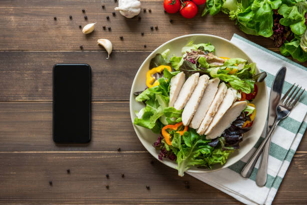 Healthy chicken salad next to smartphone on wood table background Healthy chicken salad next to smartphone on wood table background - mobile food ordering concept green leaf lettuce stock pictures, royalty-free photos & images