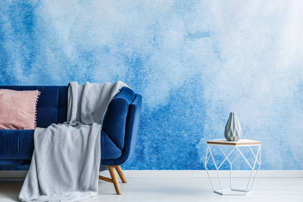 istock Contemporary openwork metal side table with vase next to a dark sofa with blanket and pillow standing against a blue and white ombre wall in a modern living room interior. Real photo. 1004109126