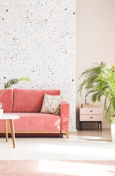 istock Plant next to pink couch with pillow in living room interior with patterned wallpaper. Real photo 1004109200