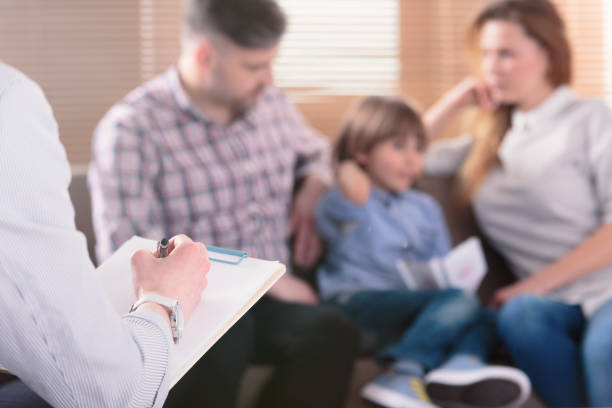 hand of a professional family psychotherapist writing notes in front of a couple with a child in a blurred background during a consultation - child therapy imagens e fotografias de stock